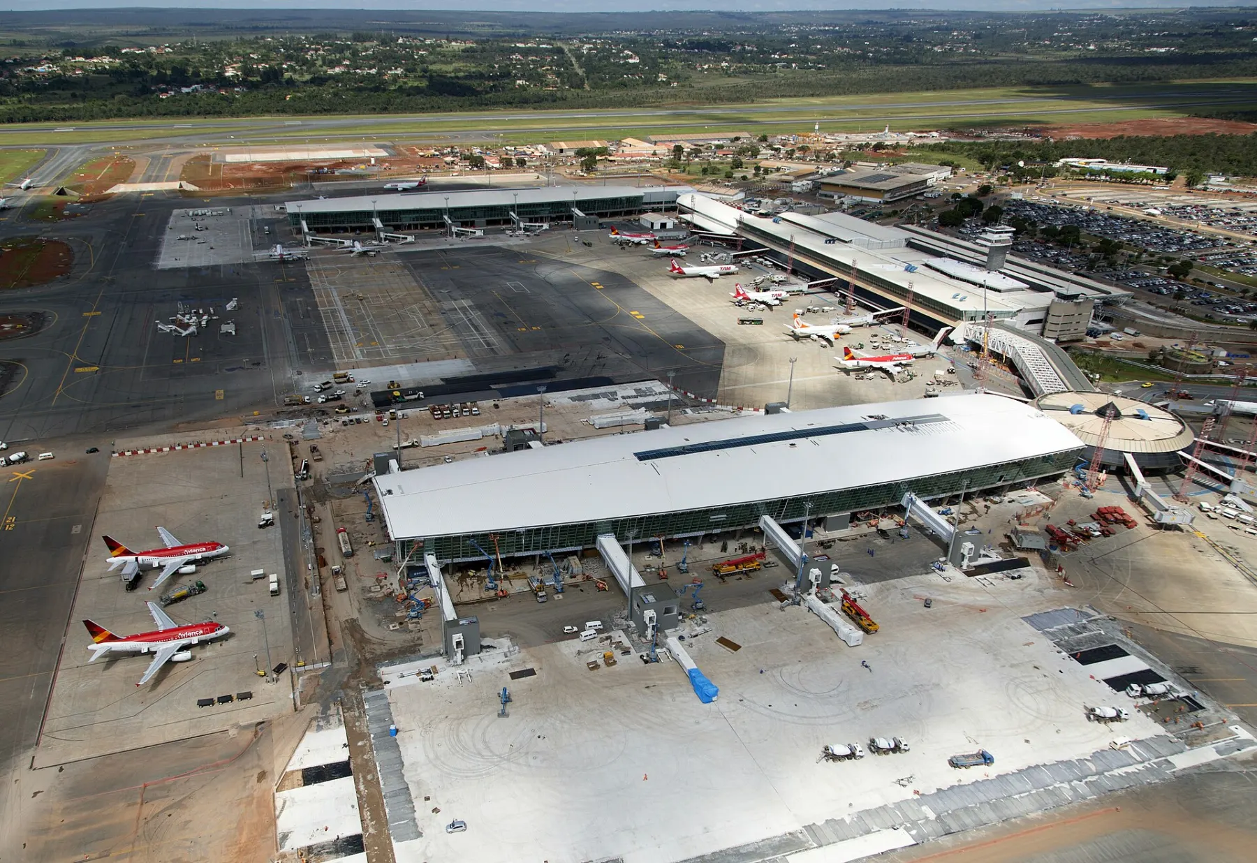 Vista aérea do Aeroporto de Brasília durante as obras de ampliação, com pátio novo de concreto e terraplenagem em terra vermelha